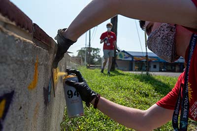 A college student sprays yellow spray paint on a concrete wall