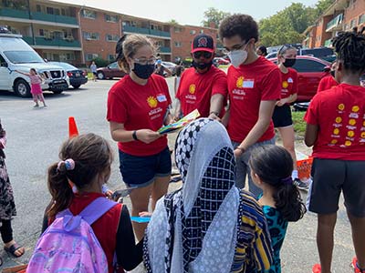 Three college students hand out school supplies to three girls