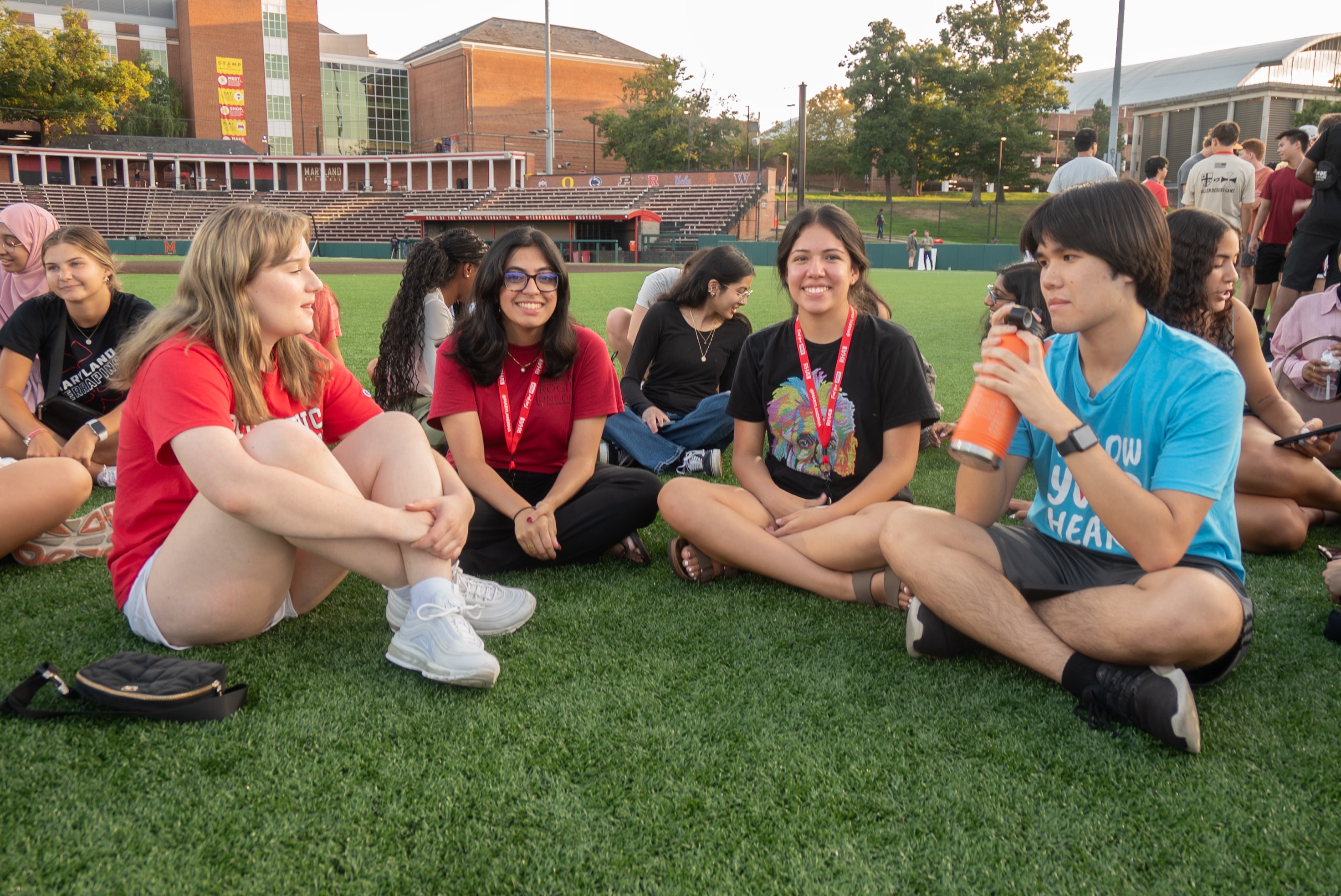 four students in a semi-circle sitting on turf smiling