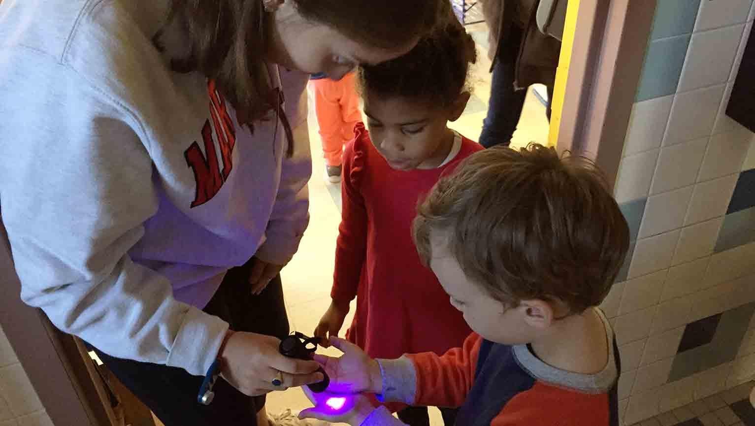 GPH scholar shining ultraviolet light on students hands