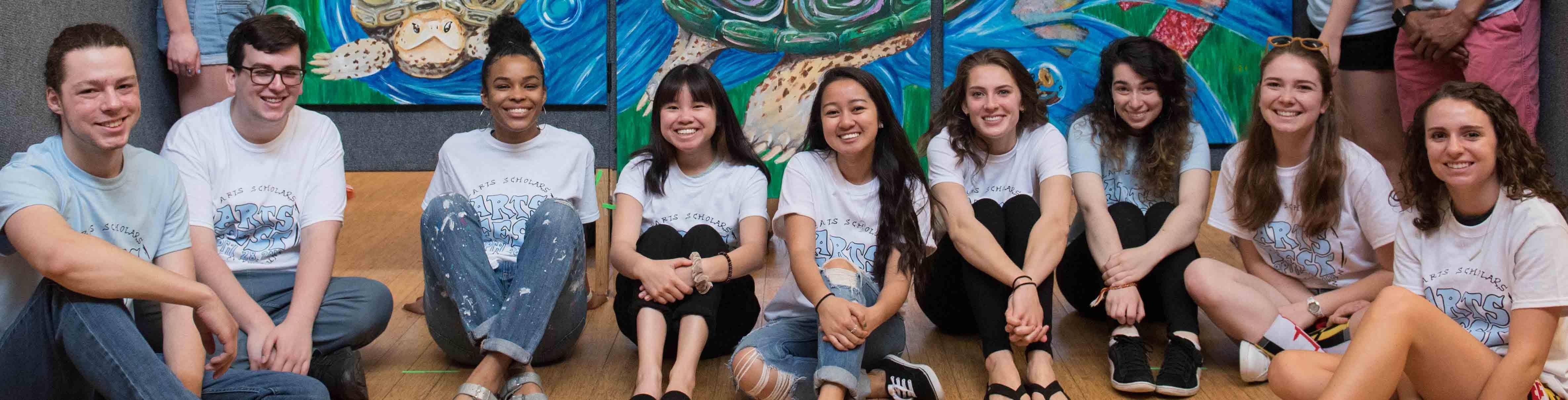 Arts students pose in front of a mural