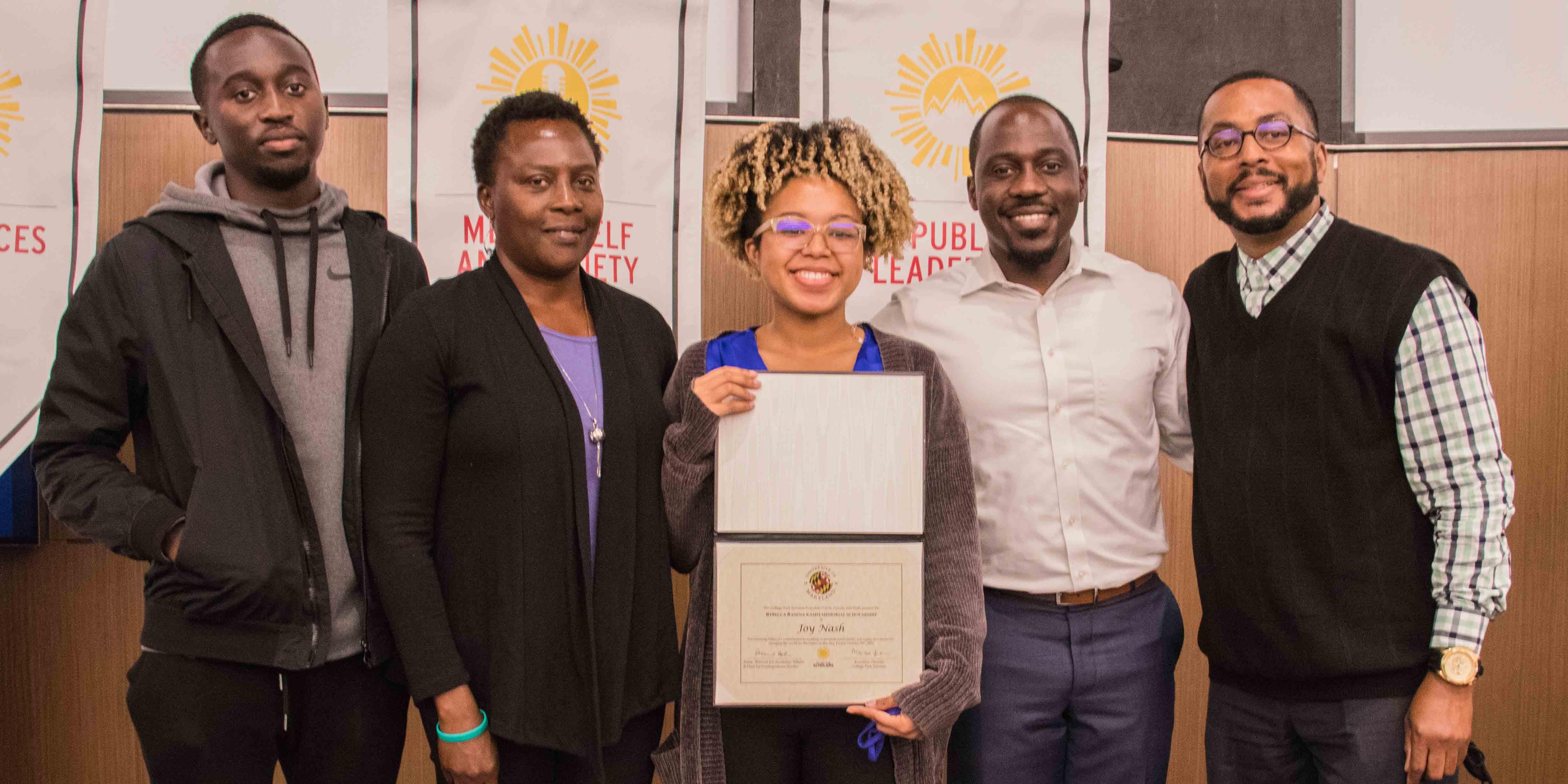 Smiling female student holding certificate stands with two people standing on either side of her