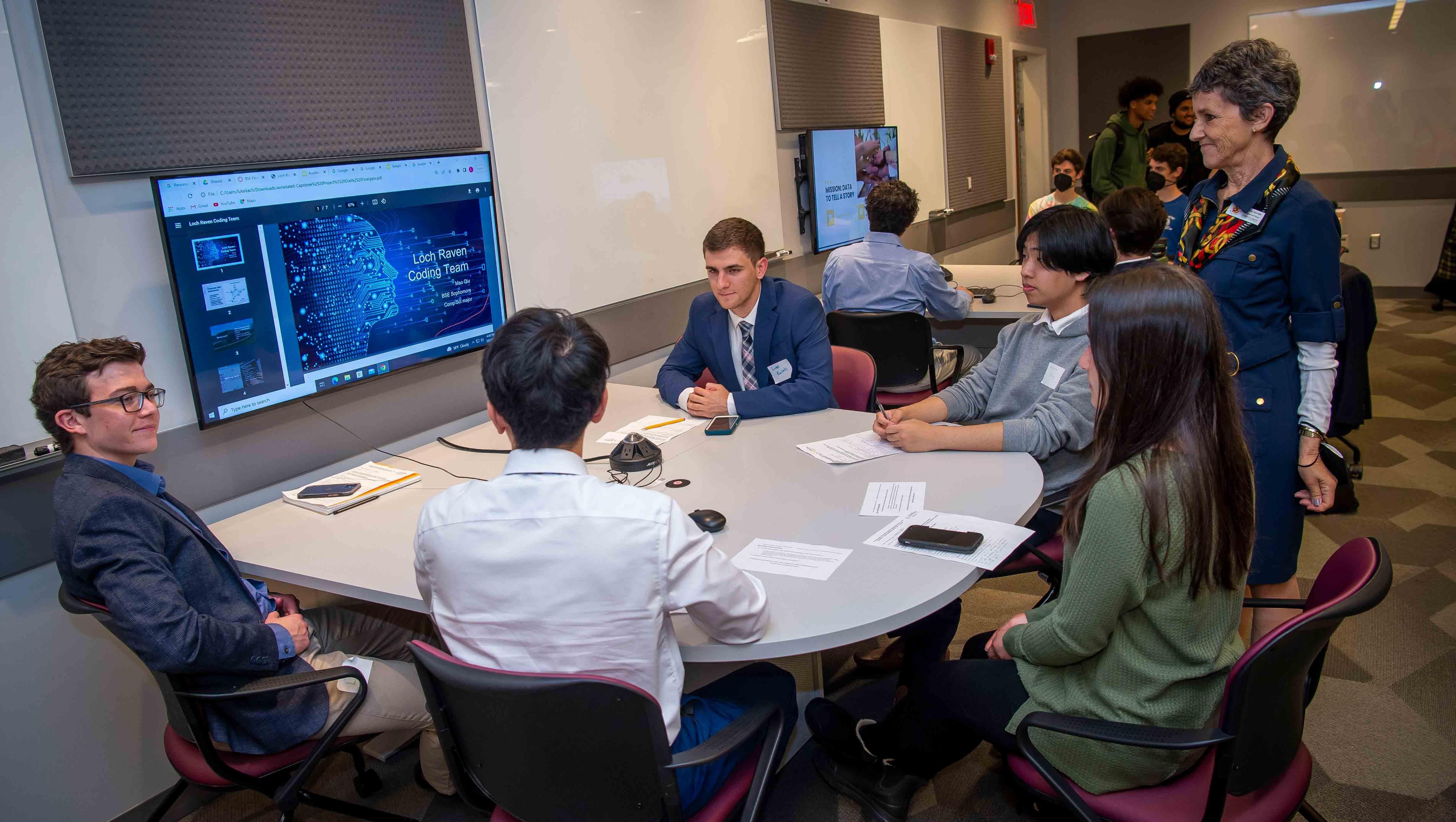 Students sitting around a TV screen take in a student PowerPoint presentation