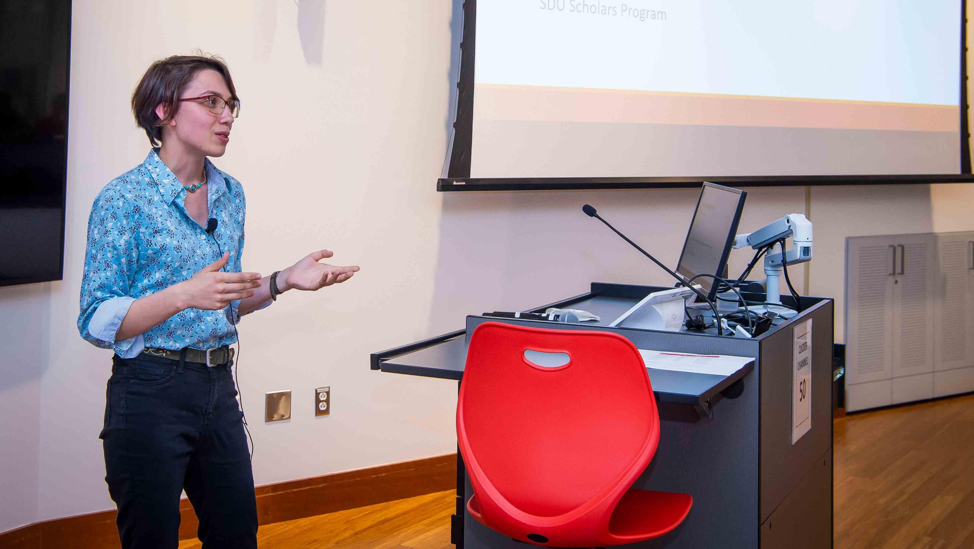 Female student standing by a screen makes a presentation