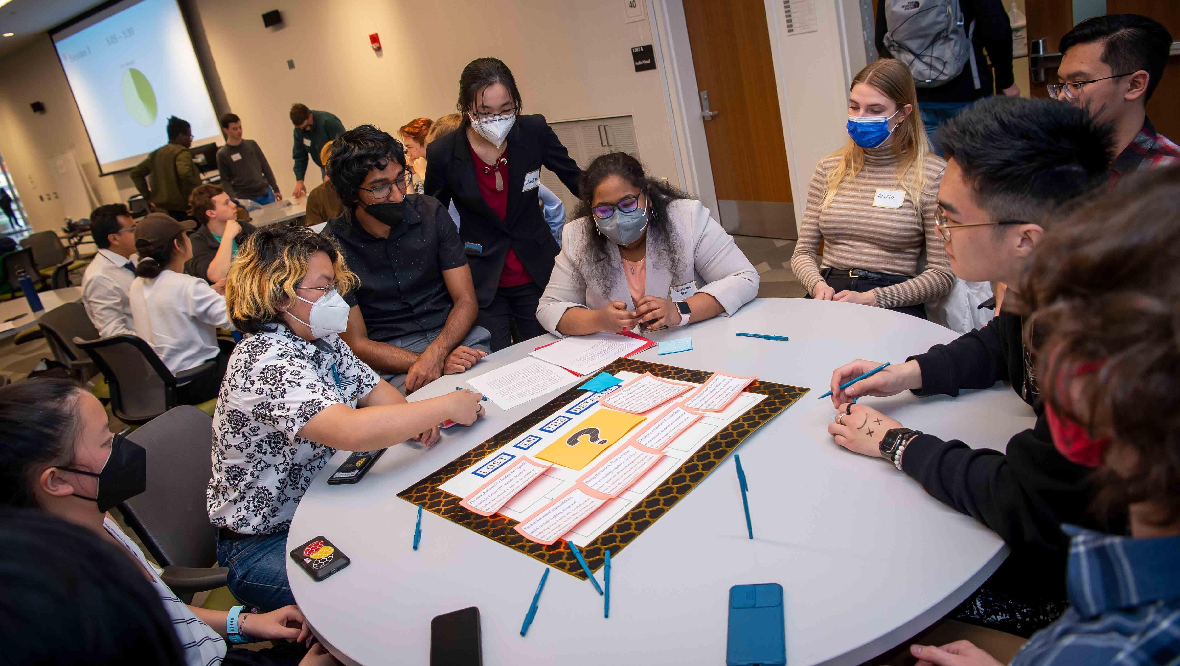 Students gathered around a table with a big boardgame-like artifact in the middle