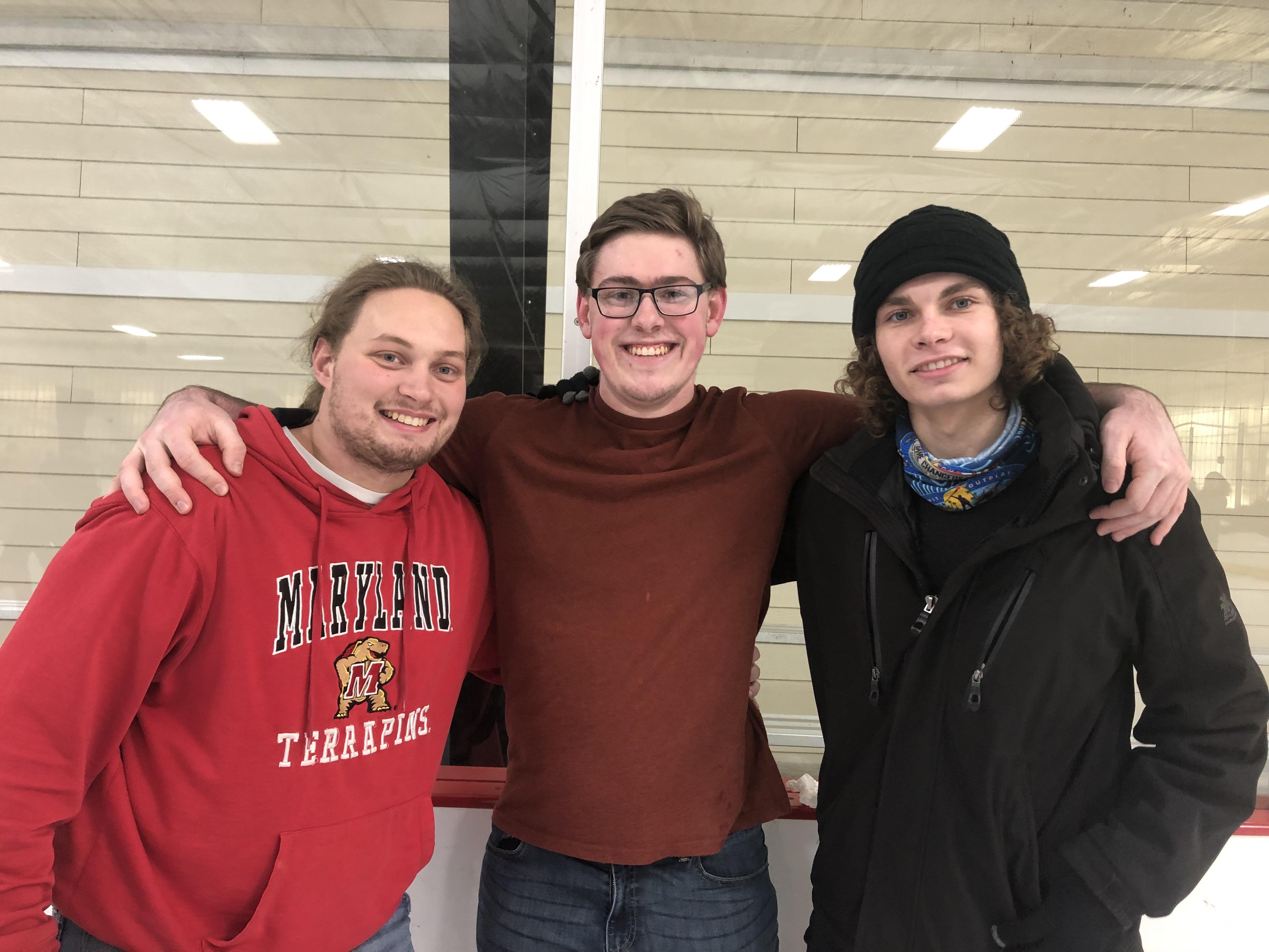 three students pose at ice rink with arms around each other