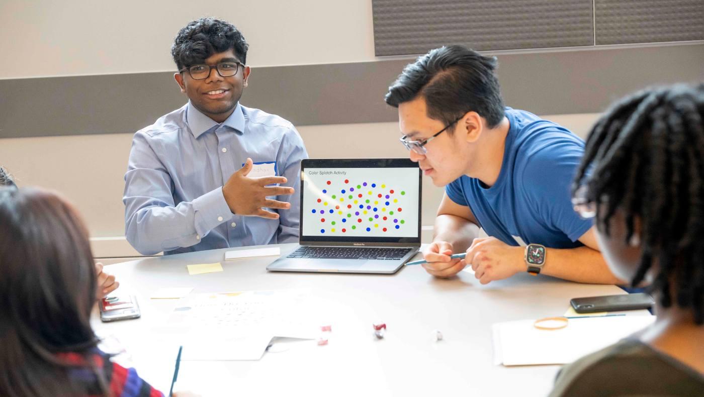 students at table look at laptop