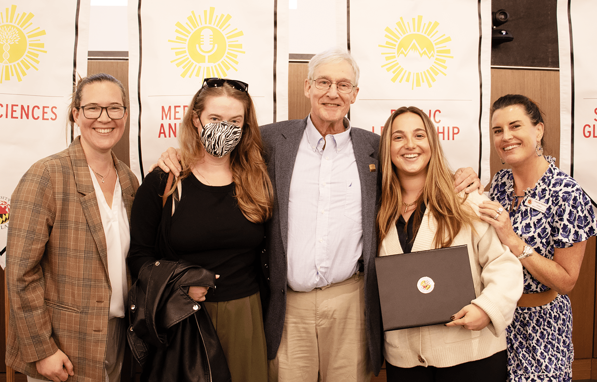 smiling award winner with faculty and award founder in front of gonfalons