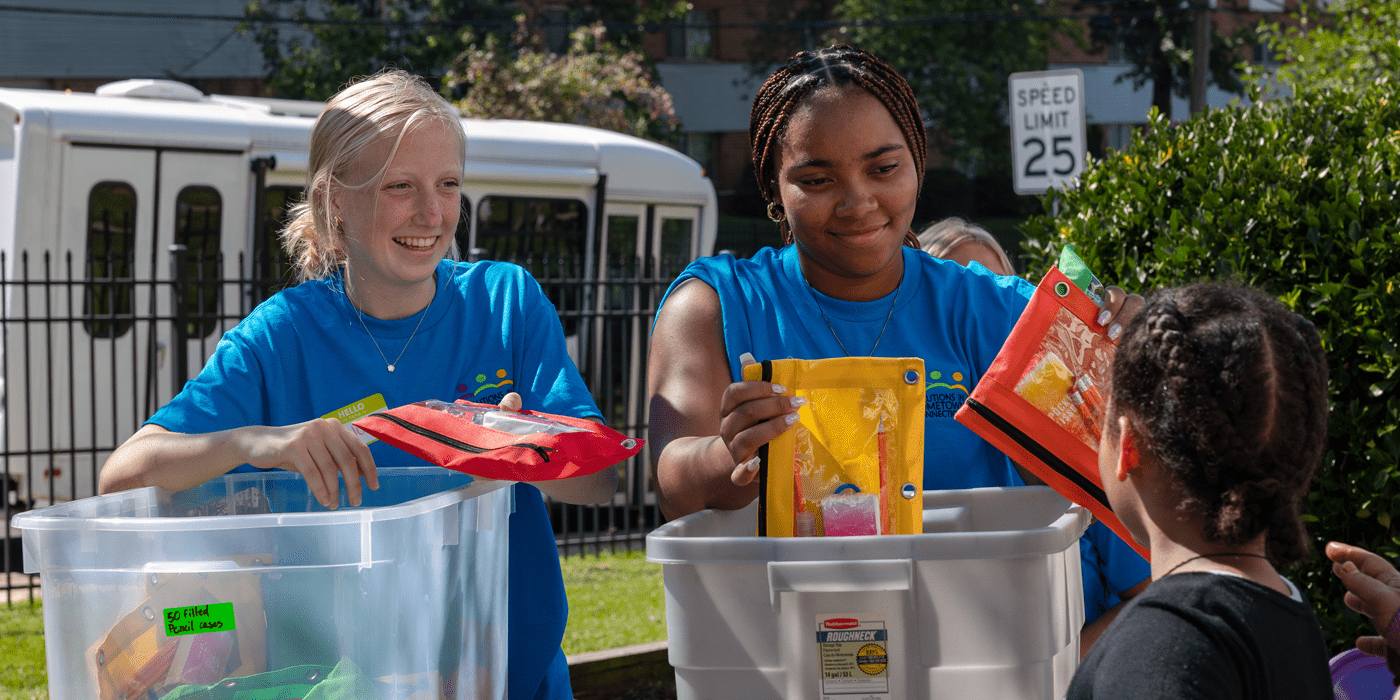 smiling volunteersbgive pencil bags to child