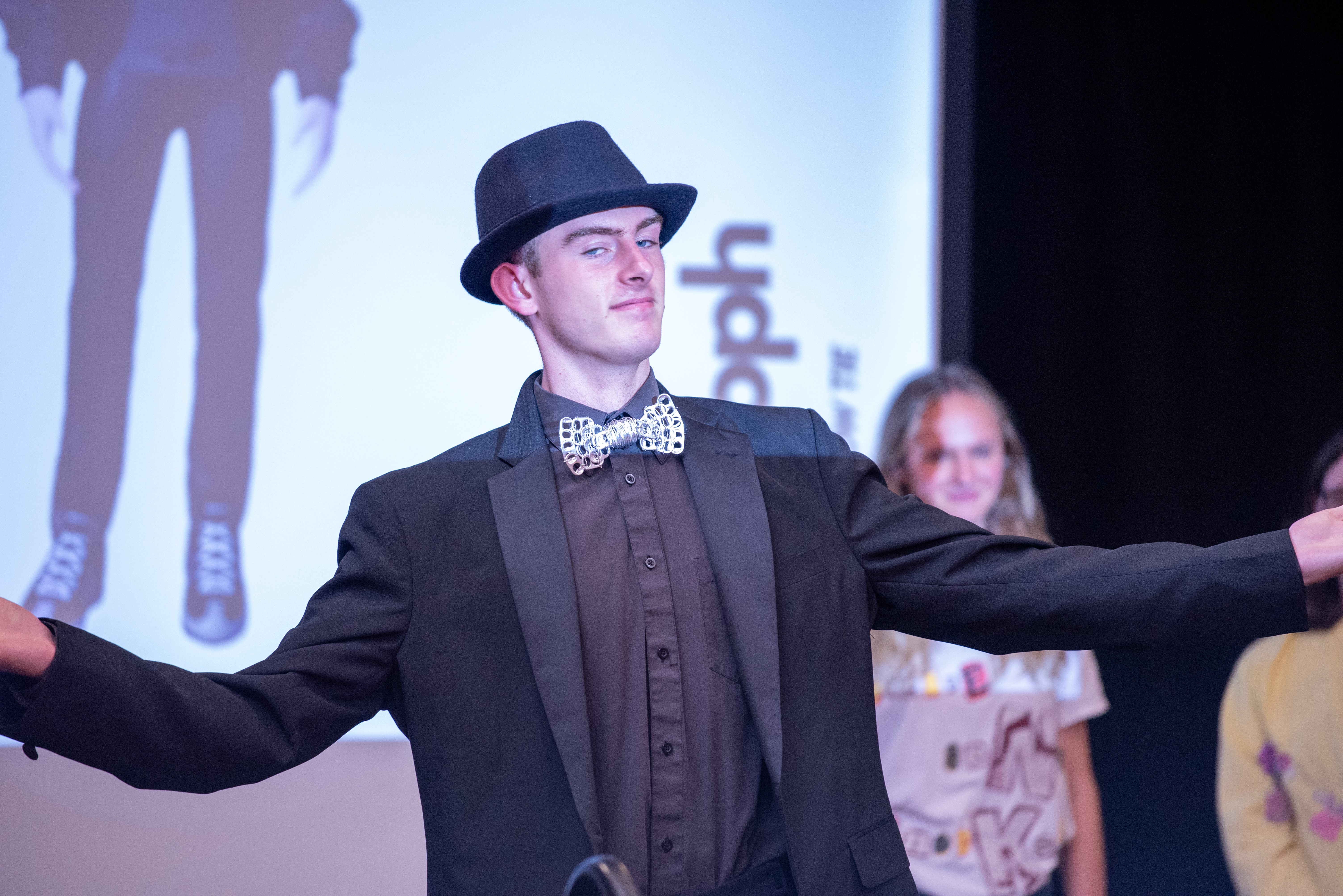 student in black hat and suit with arms extended
