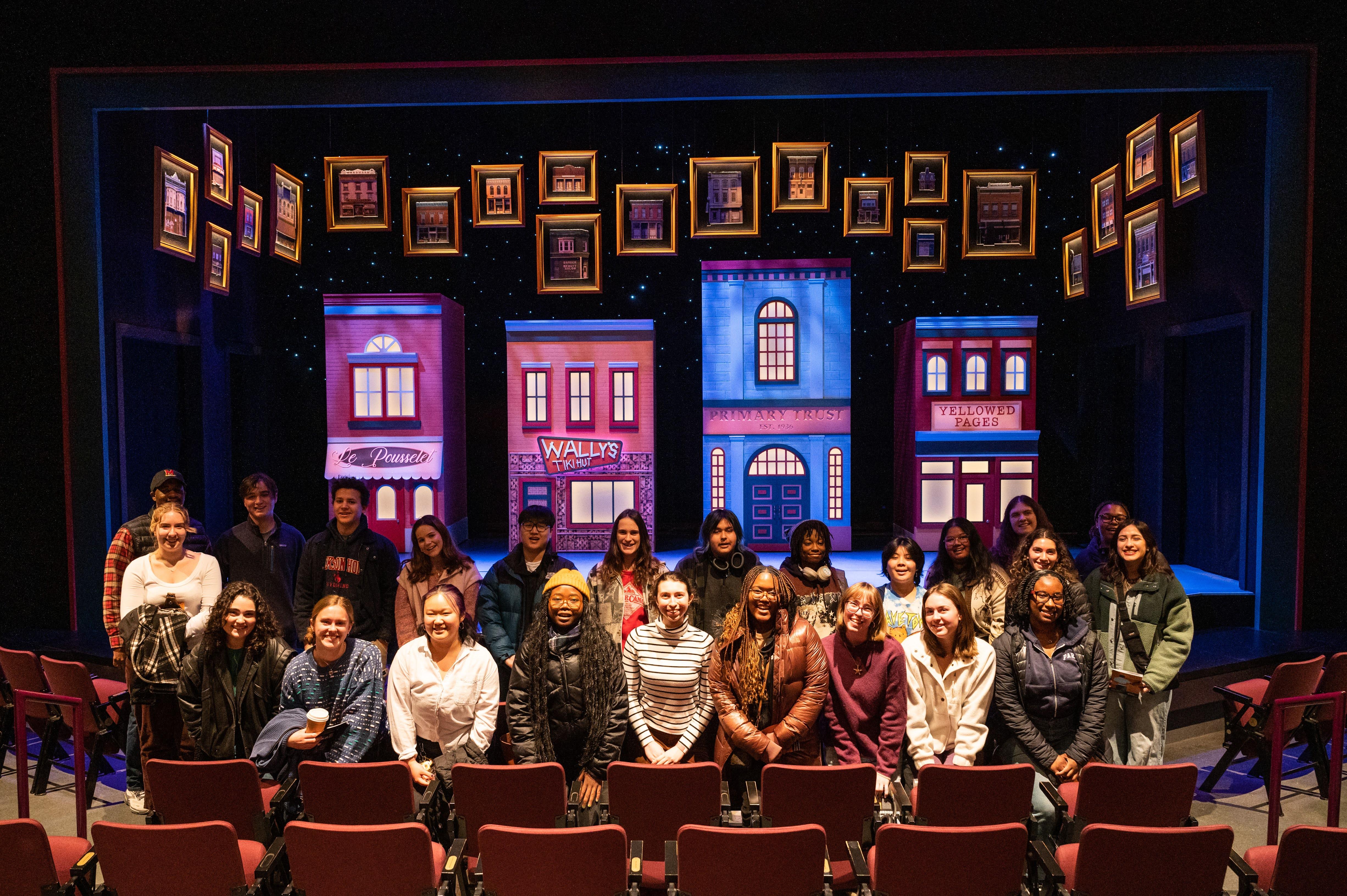 two rows of students smiling while standing in front of stage for a play
