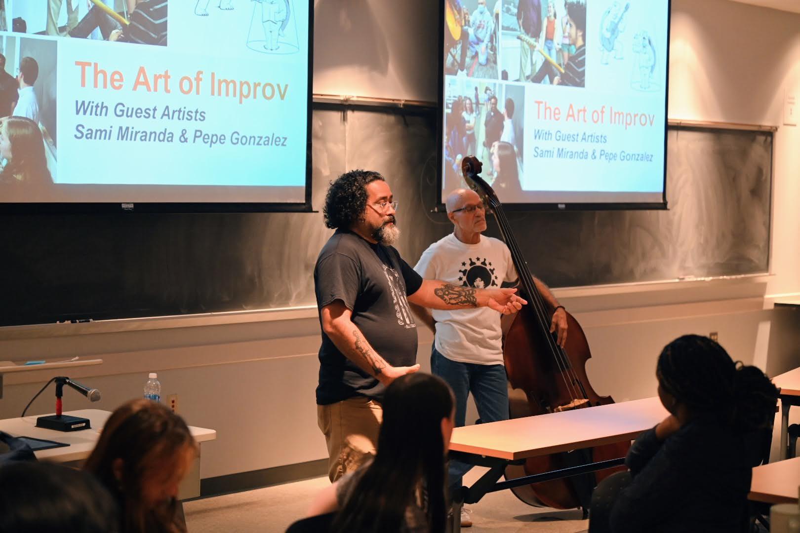two male speakers standing in front of video screens in a classroom