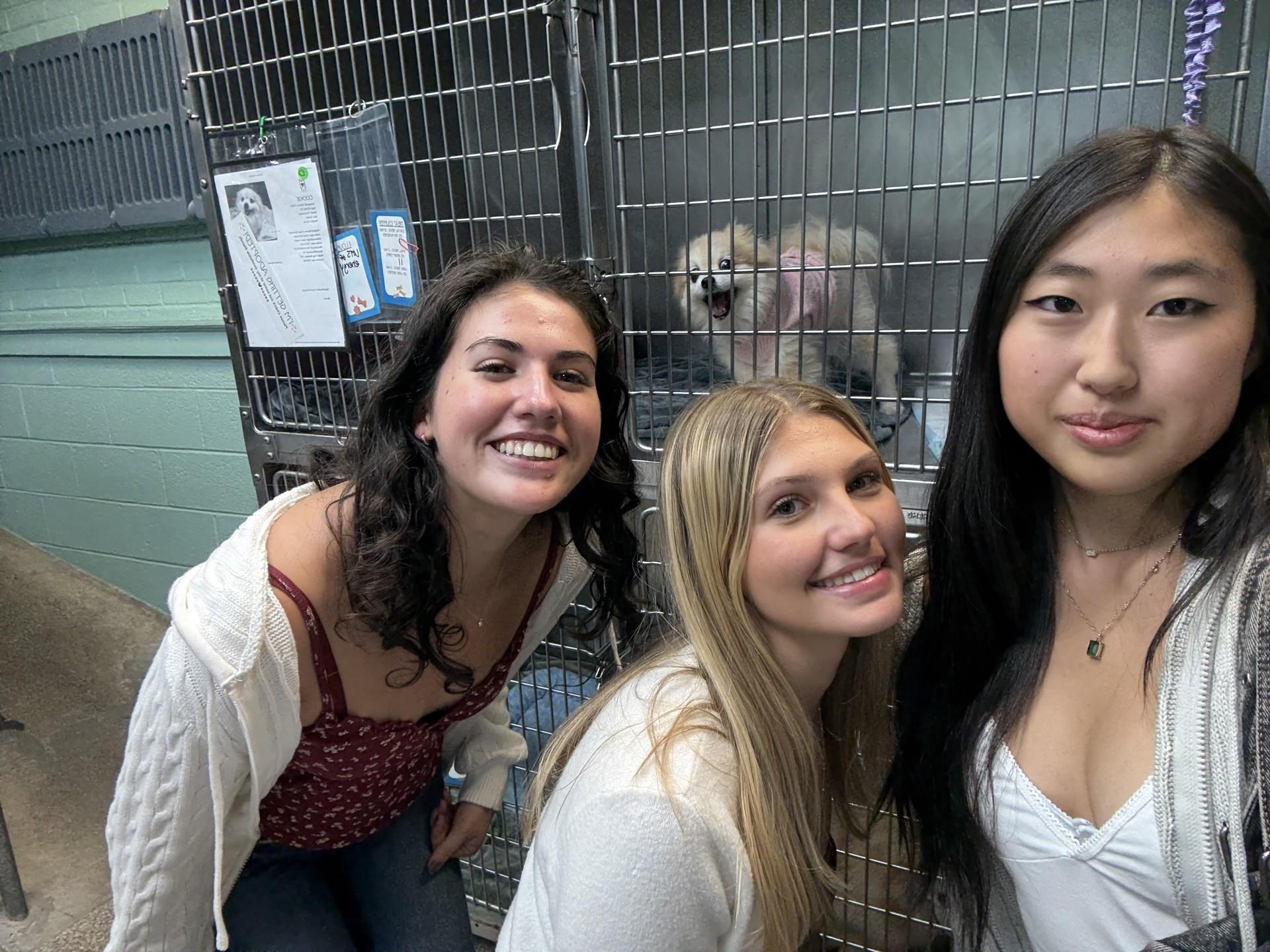 group of women smiling standing in front of a dog in kennel 