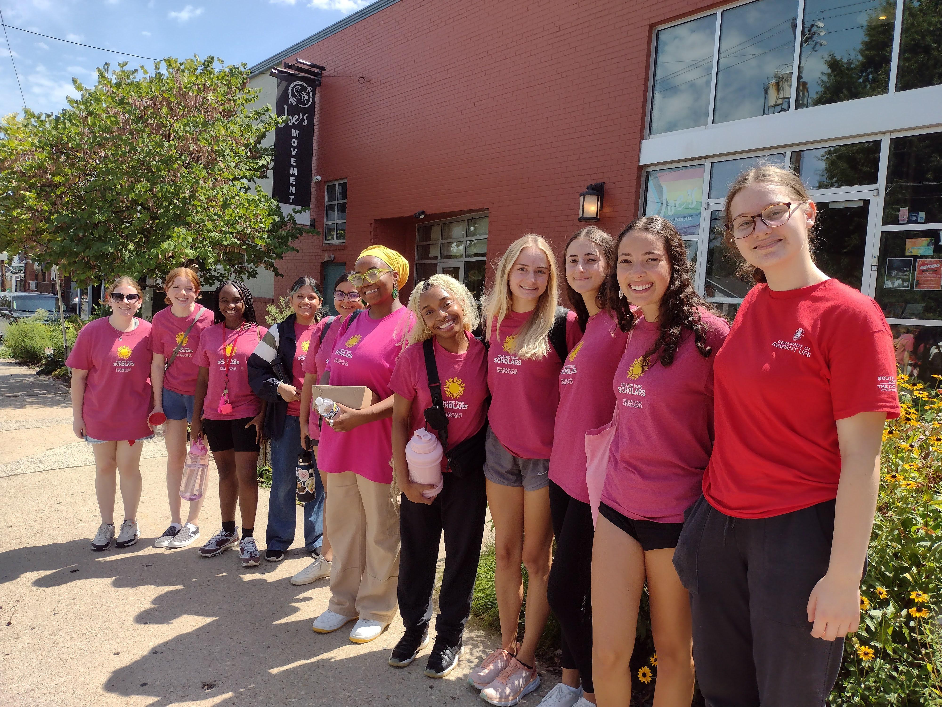 smiling students in a line in front of red brick building and flowering trees