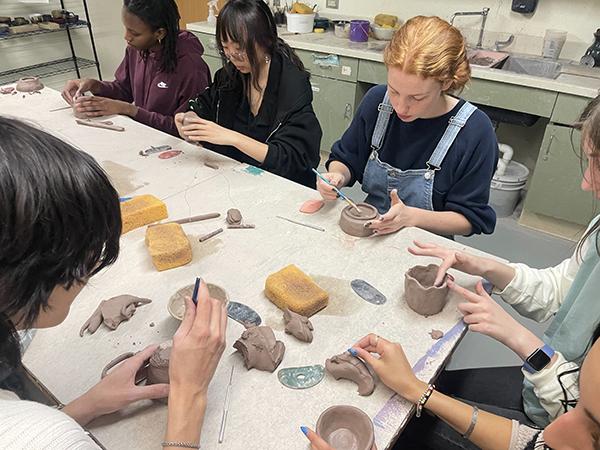 students seated around white table working with gray clay