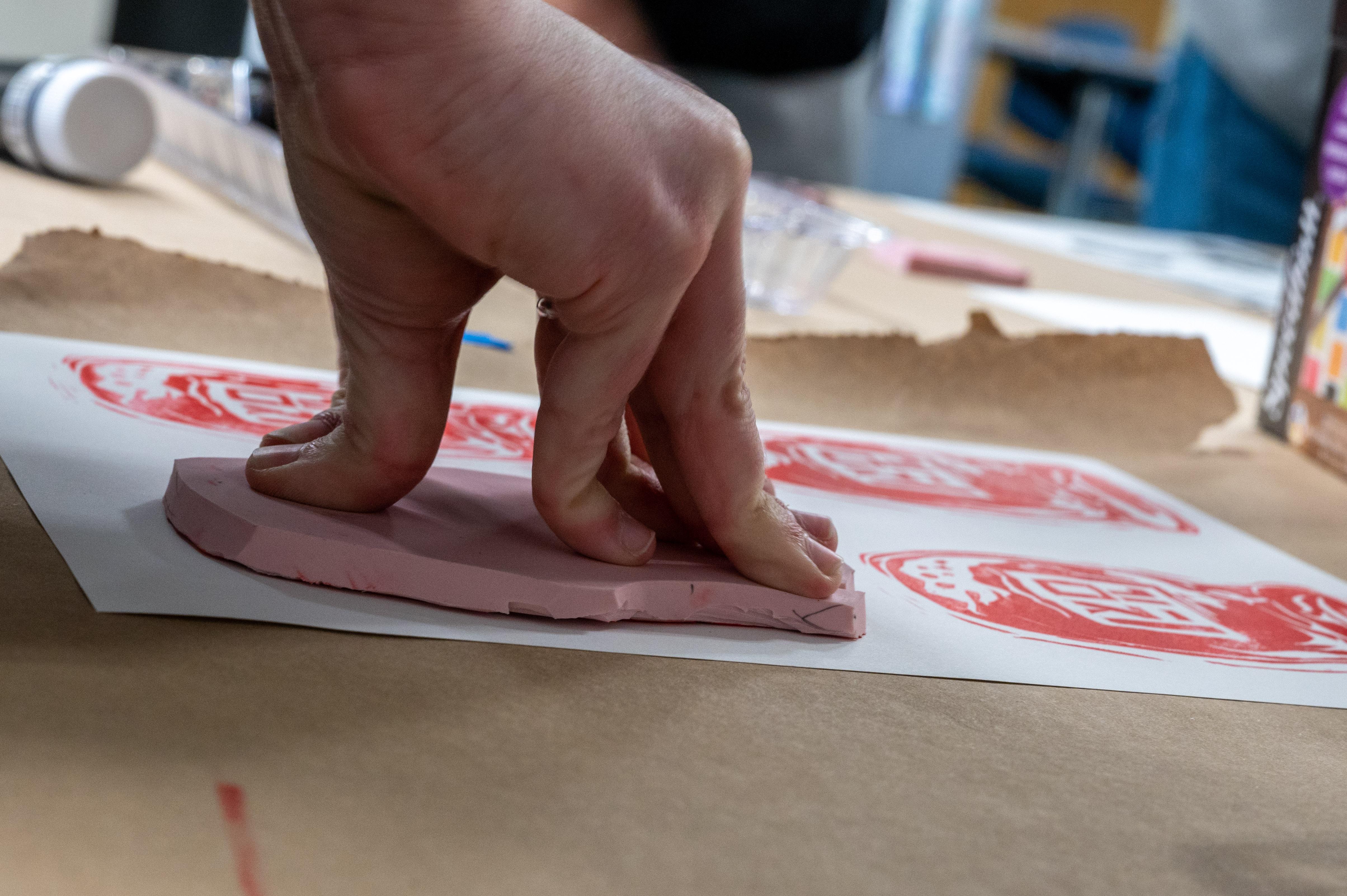 student hand pressing down on a pink stencil on white paper with red marks