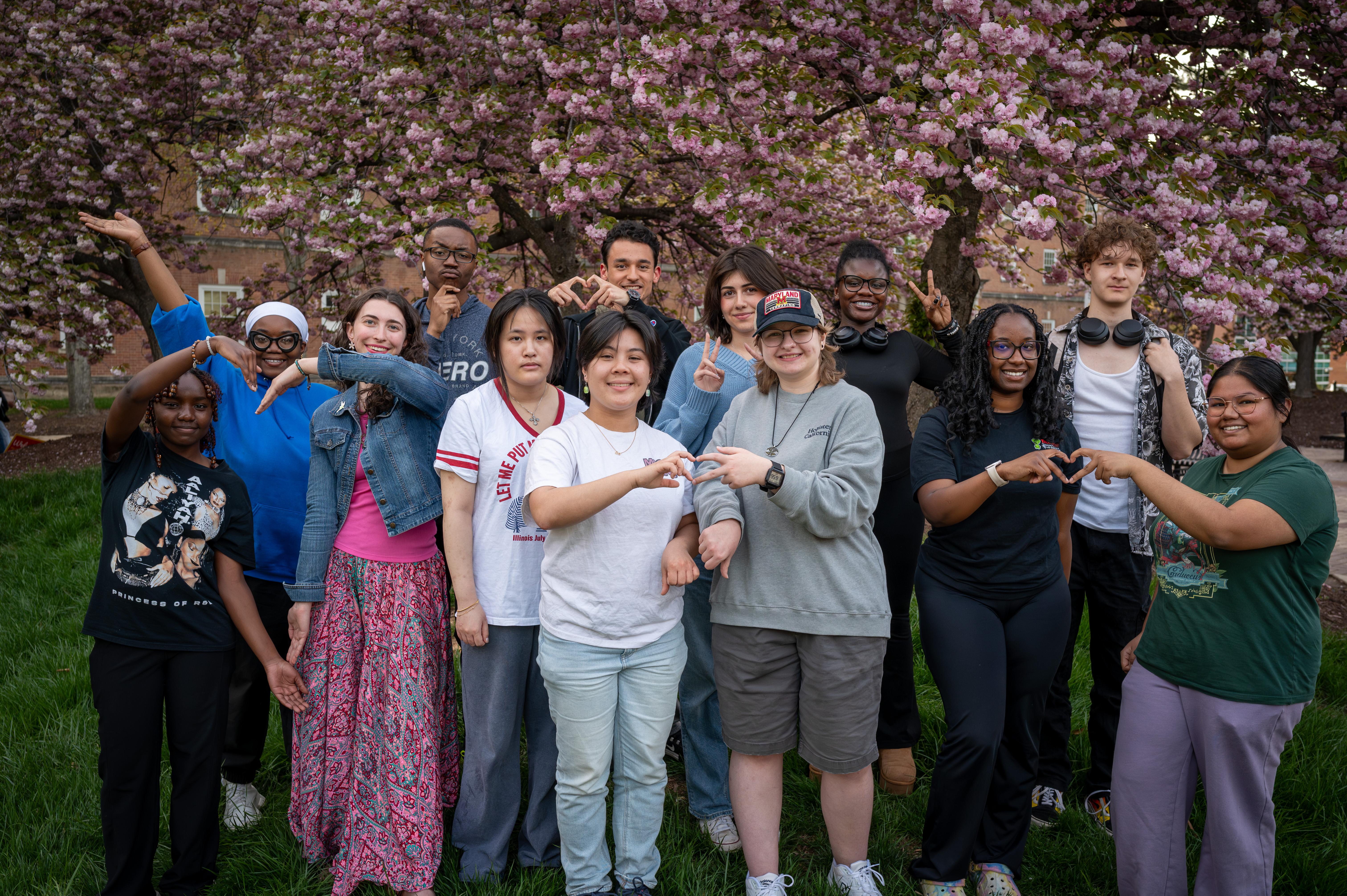 students making heart sign with hands in front of pink blooming cherry blossom tree