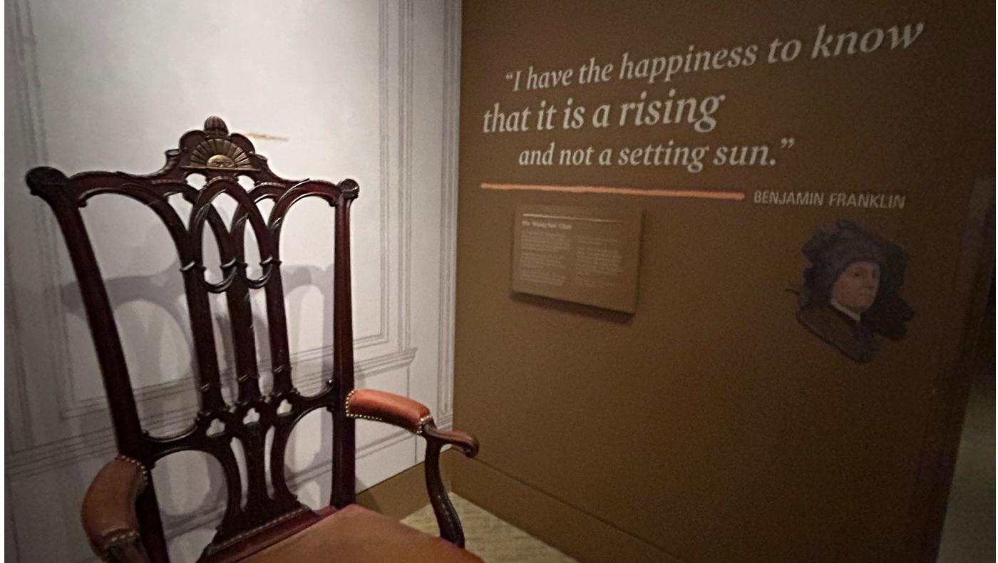 benjamin franklin quote on a brown wall near an antique chair