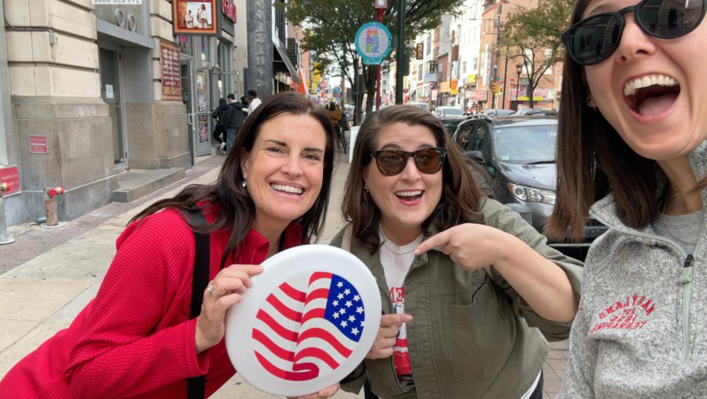 three women smilng holding a white frisbee with an American flag on it