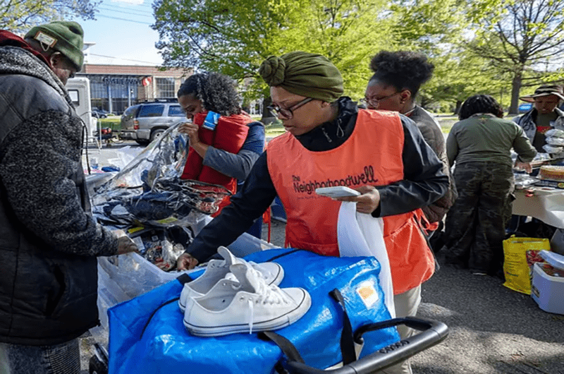 woman in orange vest, holding a bag, sorts toiletries with a man in a green hat and black coat