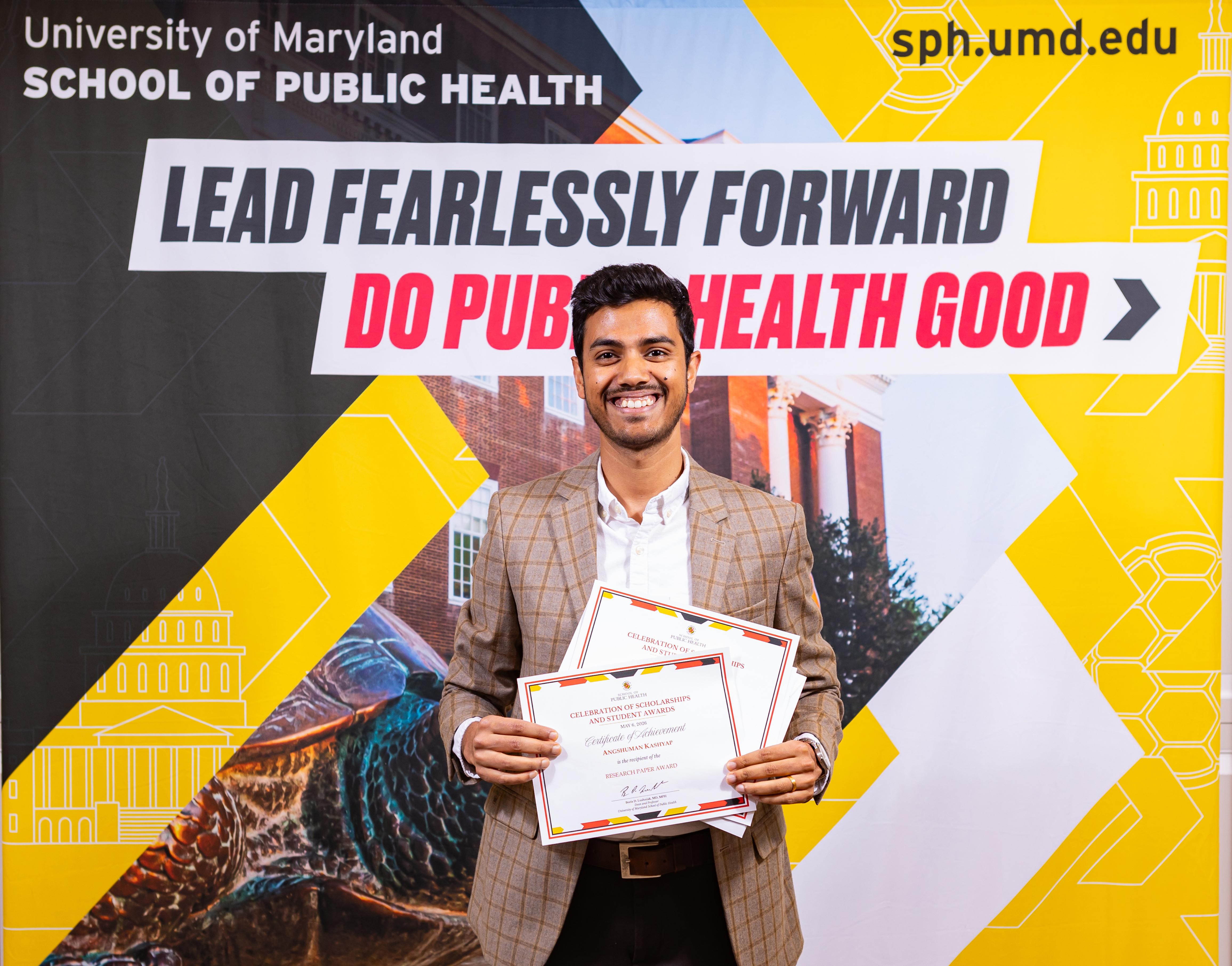 man in tan jacket holding a certificate in front of a sign