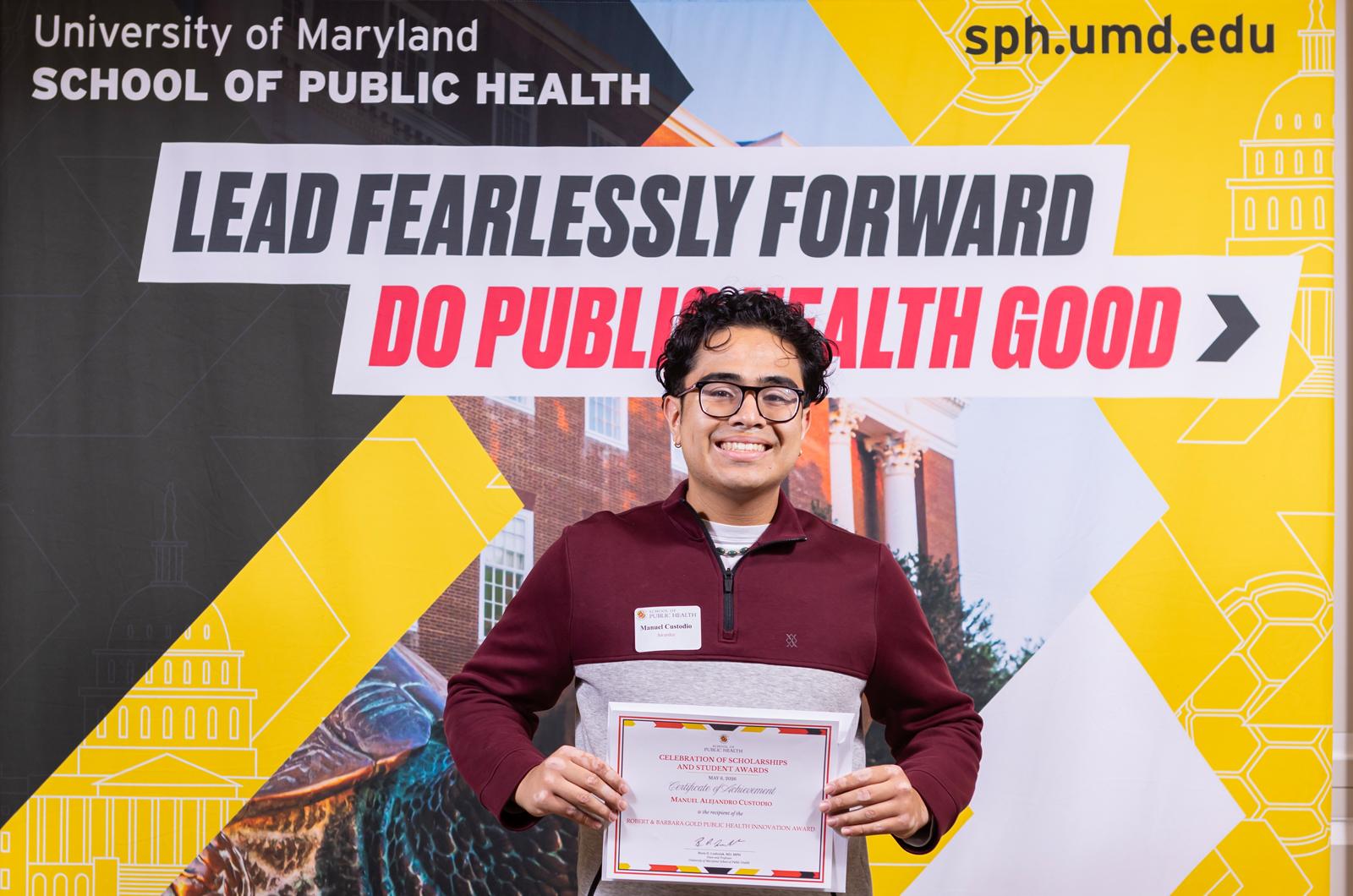 man in red shirt holding a certificate in front of a sign