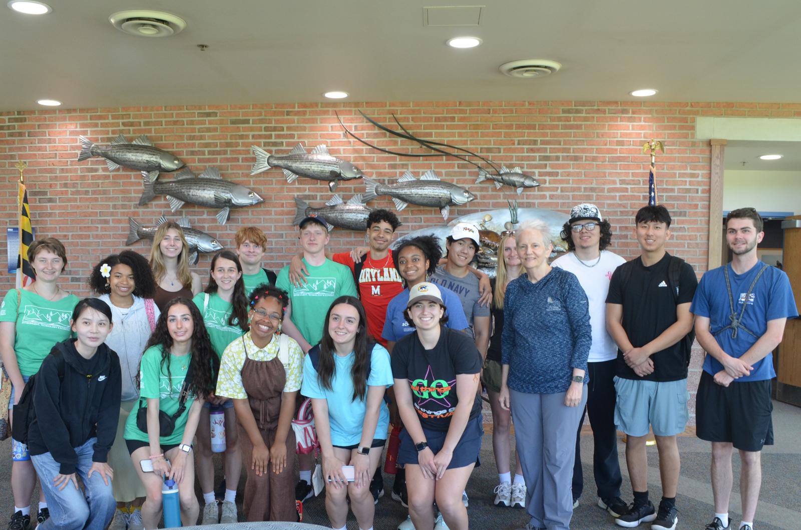 students and staff smile in front of wall with silver sculptures