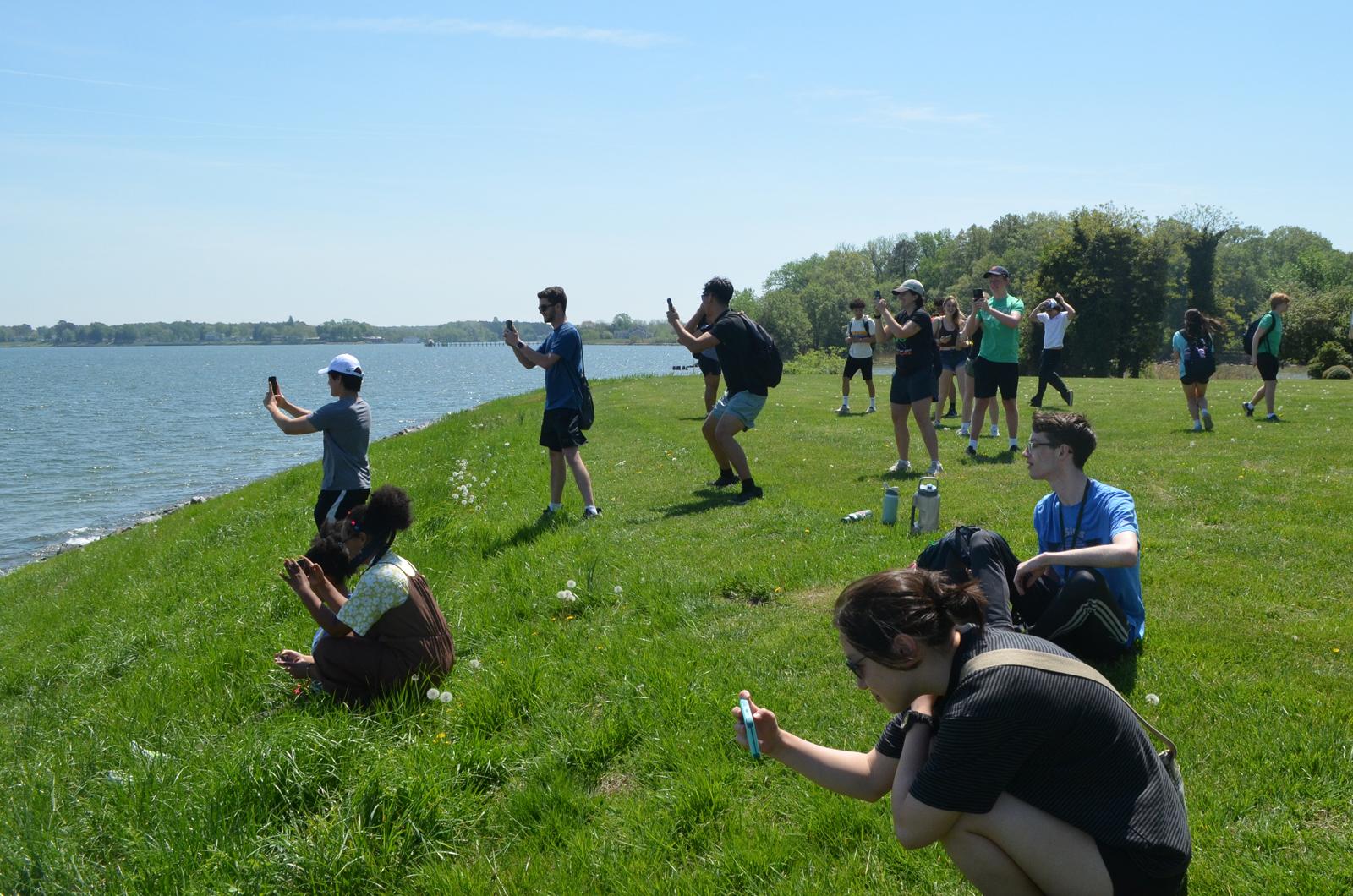 students with phones out on a grassy hill overlooking water