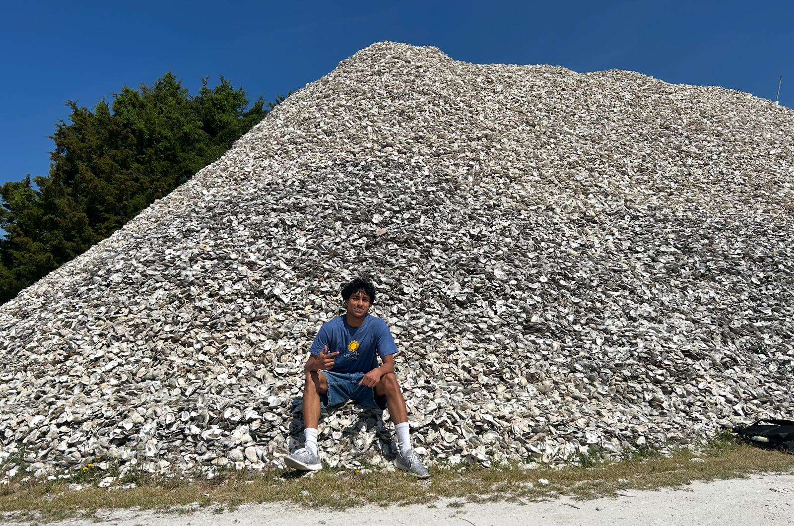 student in blue shirt sitting on a pile of oyster shells