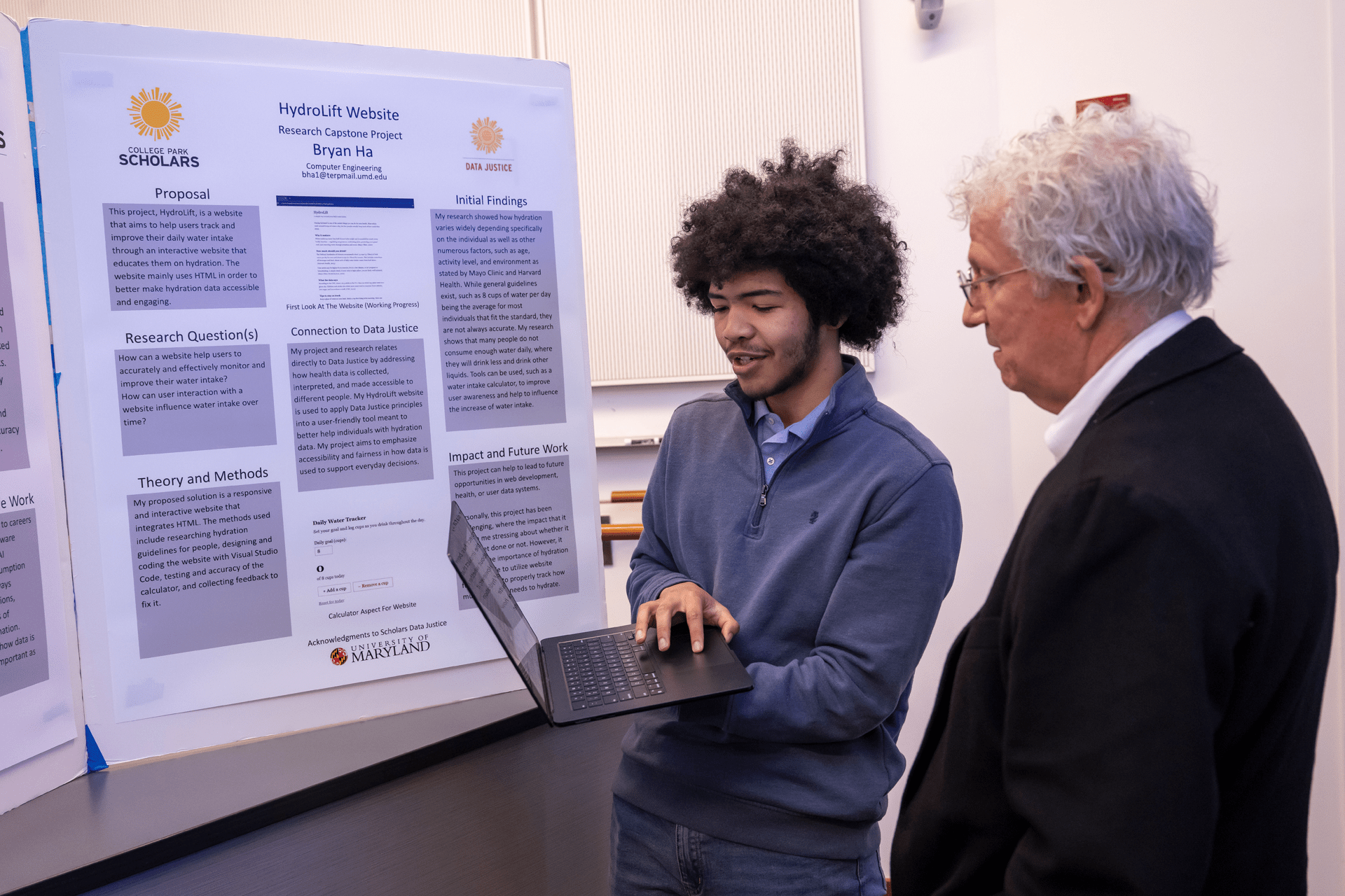 student showing laptop screen to man with white hair
