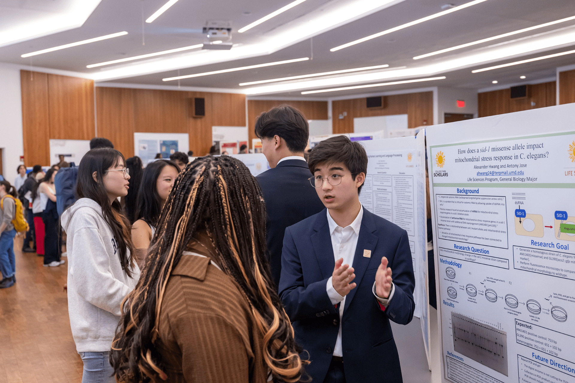 student in blue jacket in front of a poster board talking to a student 