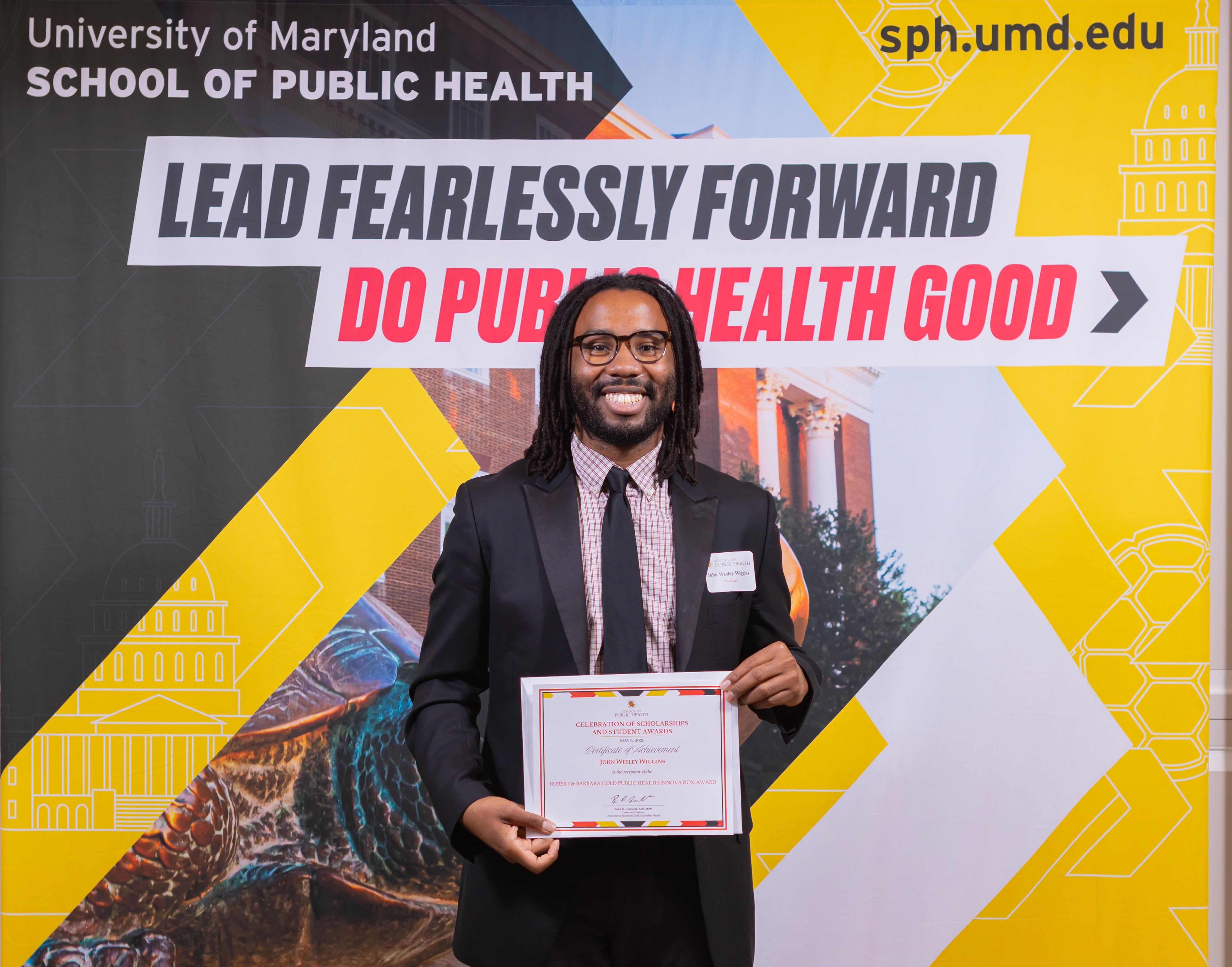 man in black suit holding a certificate in front of a sign